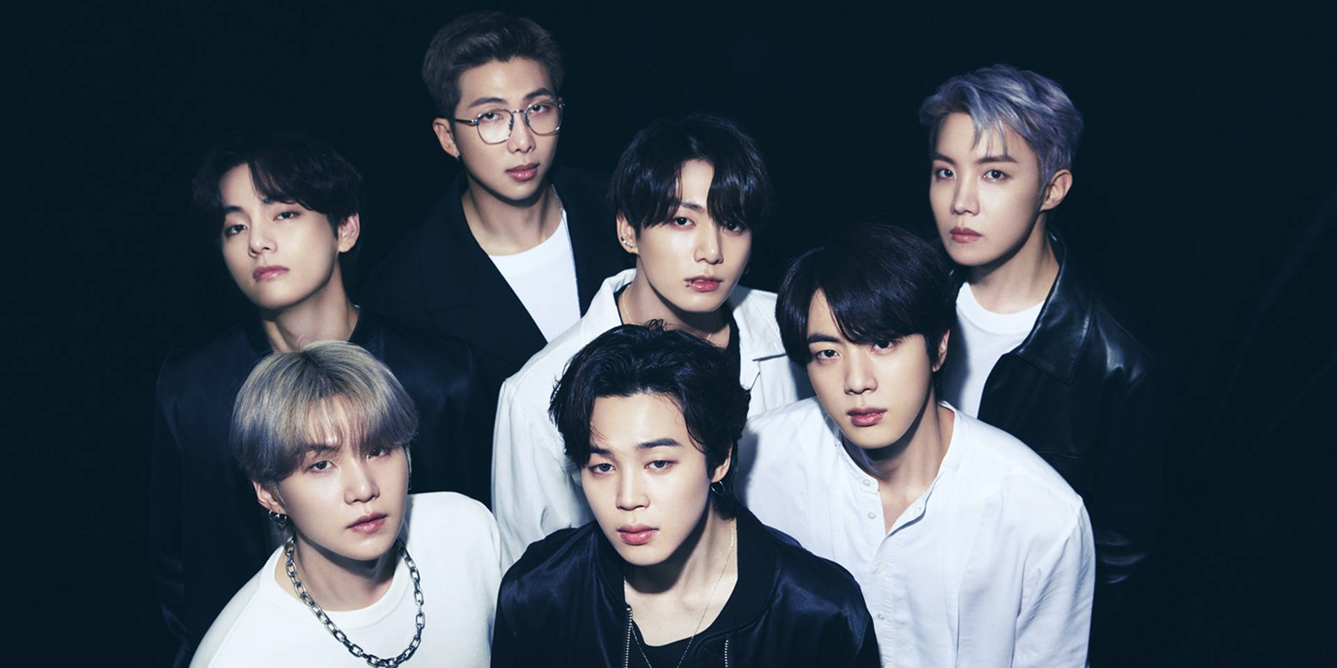BTS 桌布 桌布 壁紙 — 七位時尚年輕男士身穿深色和白色服裝，在黑色背景前自信擺姿勢，配以戲劇性燈光。