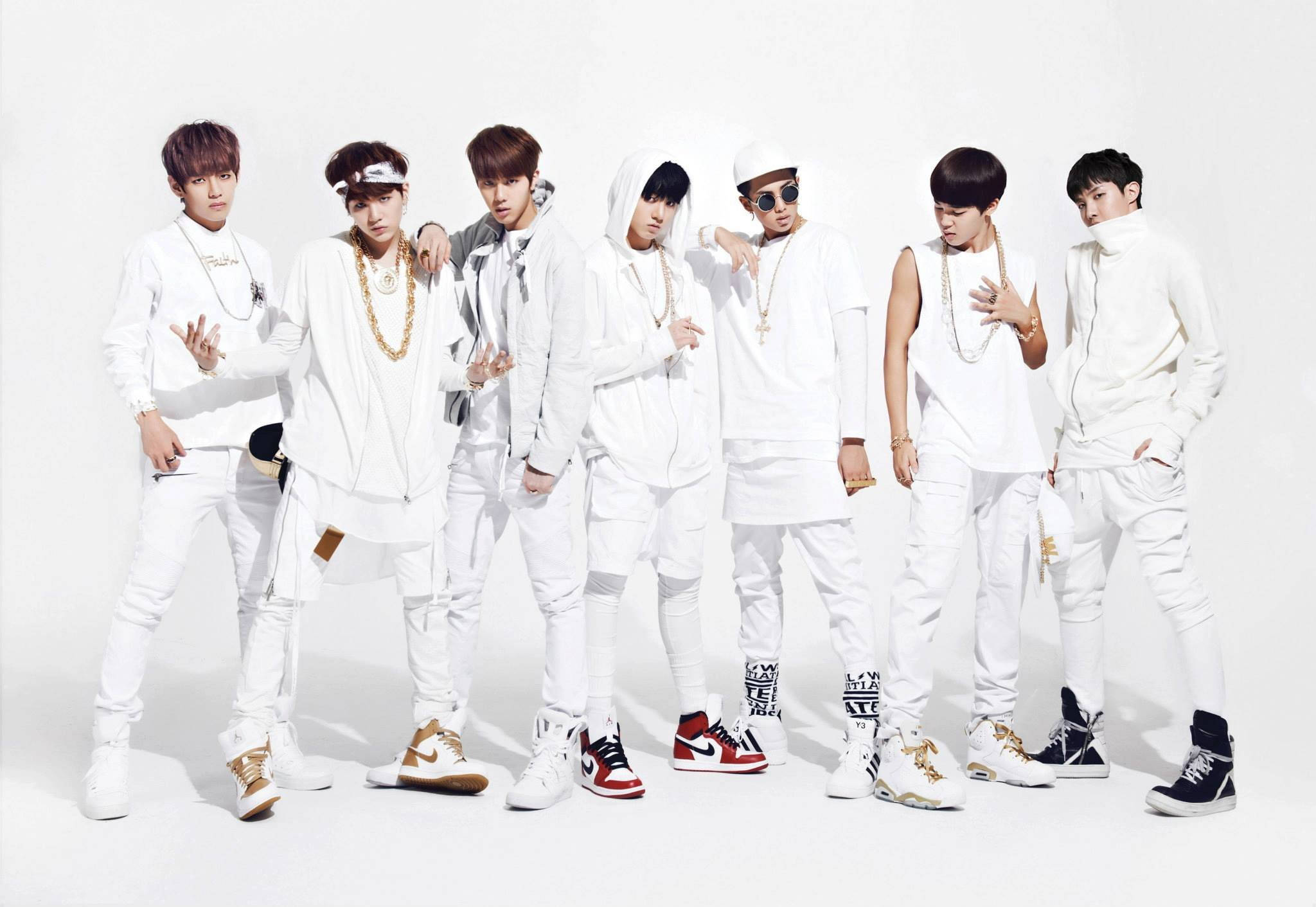 BTS 桌布 壁紙 — 七位時尚年輕男士身穿白色服裝，佩戴金色飾品和色彩繽紛的運動鞋，在純白背景前自信地擺姿勢。