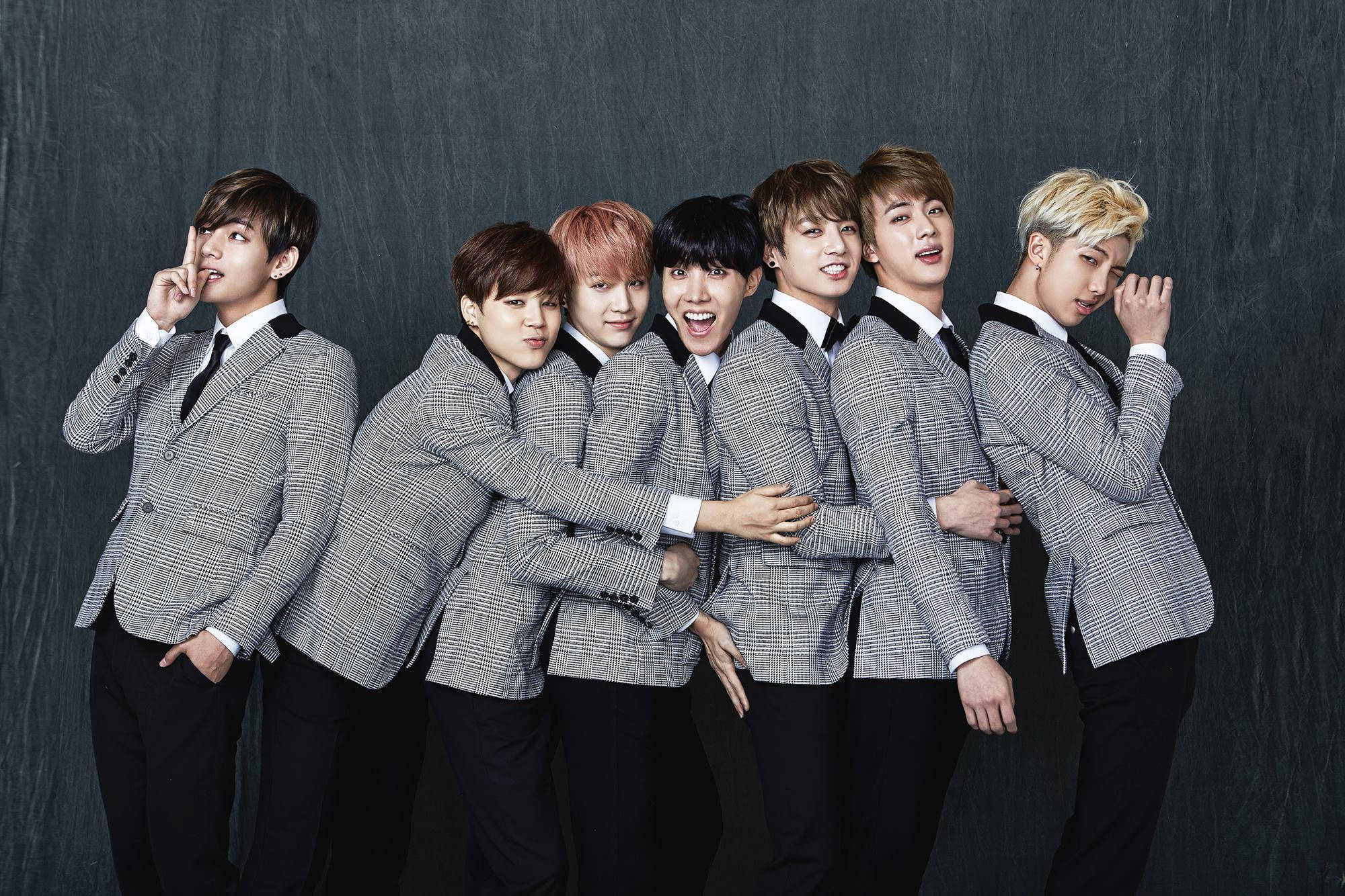BTS 2021 桌布 壁紙 — 七位時尚年輕男士身穿相配的灰色格子西裝，在深色紋理背景前俏皮地擺姿勢。