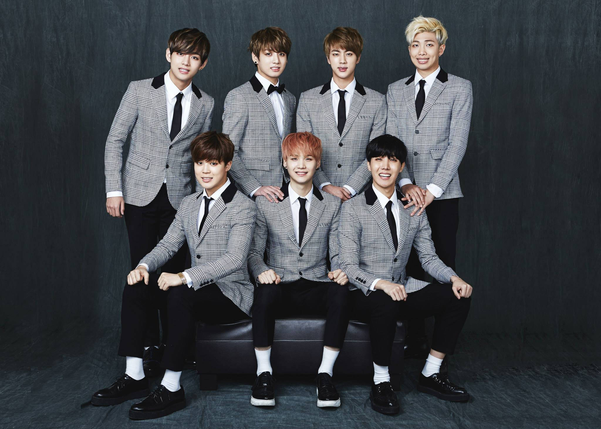 bts 2021 desktop 桌布 壁紙 — 七位時尚年輕男士身穿相配的灰色格紋西裝，自信地坐在黑色長椅上，背景是深色紋理。