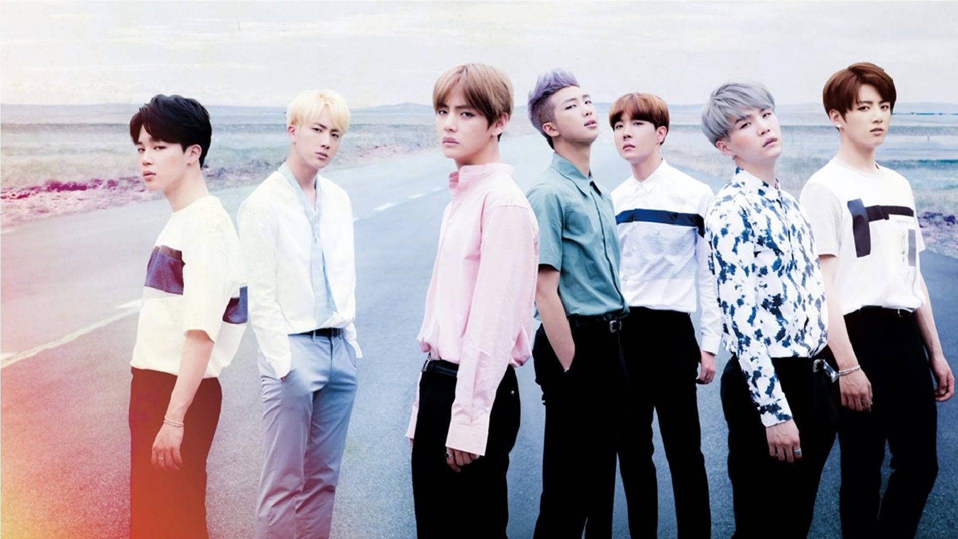 BTS 2021 桌布 壁紙 — 七位時尚年輕男士身穿色彩繽紛的襯衫，自信地站在沙漠公路上，天空呈現柔和粉彩色調。