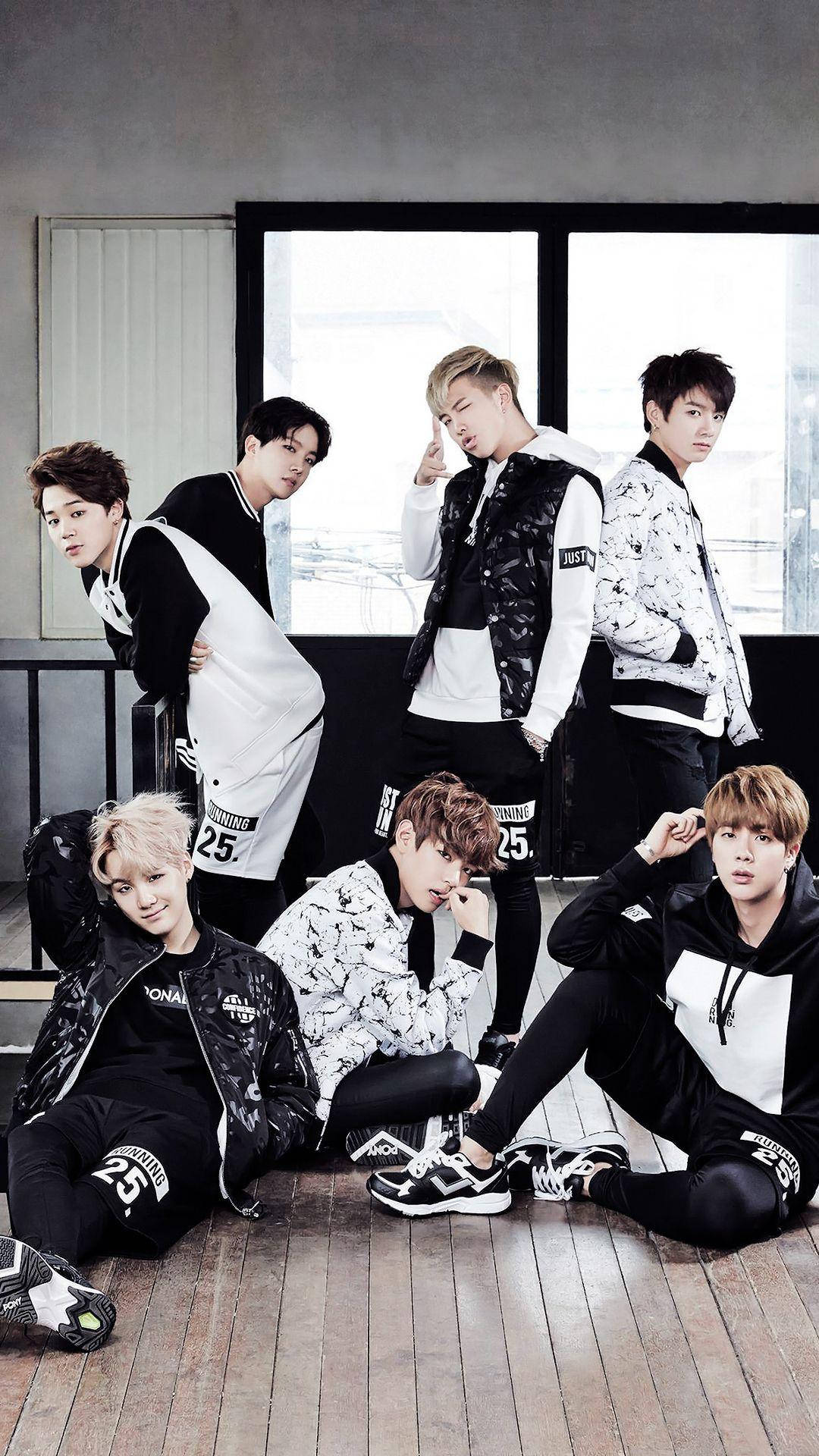 BTS 鎖定螢幕 桌布 壁紙 — 七位時尚年輕男士身穿黑白街頭服飾，在木地板上靠近大窗戶自信地擺姿勢。