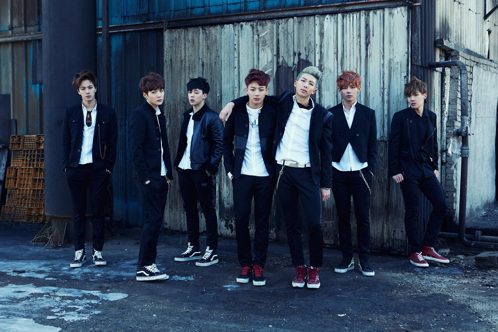 BTS 桌布 壁紙 — 七位時尚年輕男士身穿黑色外套和白色襯衫，在風化的工業牆前自信地擺姿勢。