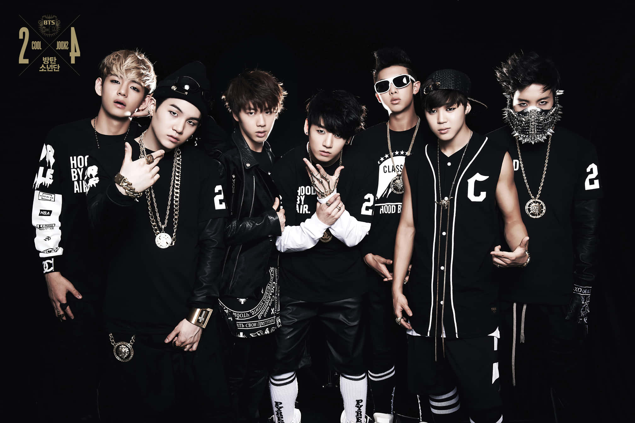 K-pop 桌布 壁紙 — 七位時尚年輕男士身穿黑色街頭服飾，在深色背景前自信擺姿勢，配以搶眼配飾和強烈表情。