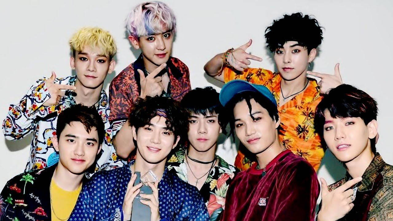 K-pop 桌布 壁紙 — 七位時尚年輕男士身著鮮豔熱帶印花和醒目髮色，在純白背景前自信擺姿勢。