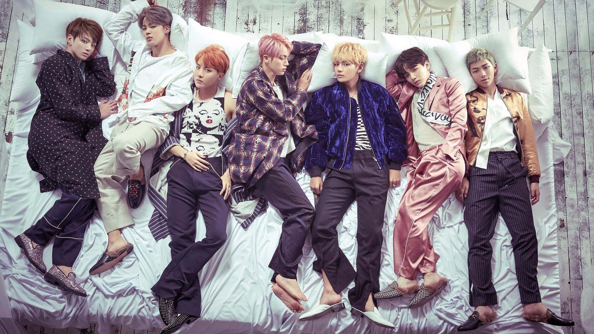 Bts Rap Monster 桌布 壁紙 — 七位時尚年輕男子在一張鋪有白色床單和枕頭的大床上休息，背景是風化的木牆。