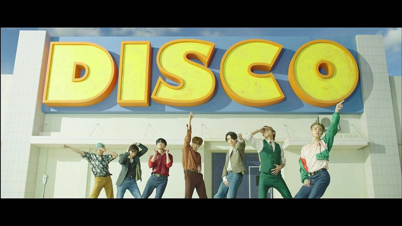 BTS 桌布 桌布 壁紙 — 七位時尚年輕男子在明亮的藍天下，於一個巨大的黃色「DISCO」標誌下擺出動感姿勢。