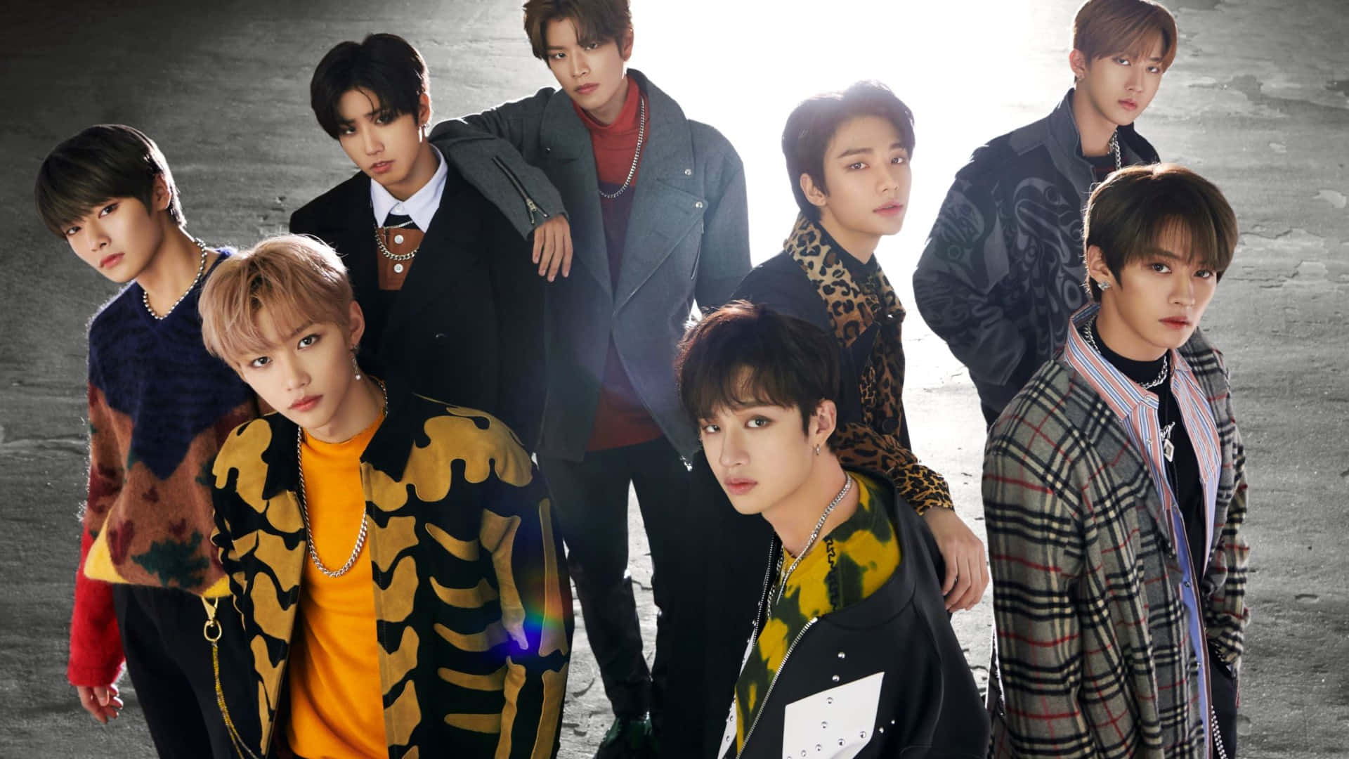 Stray Kids 2020 桌布 壁紙 — 七位時尚年輕男子穿著大膽街頭服飾，在粗糙的混凝土背景前自信擺姿勢，帶有戲劇性的背光。