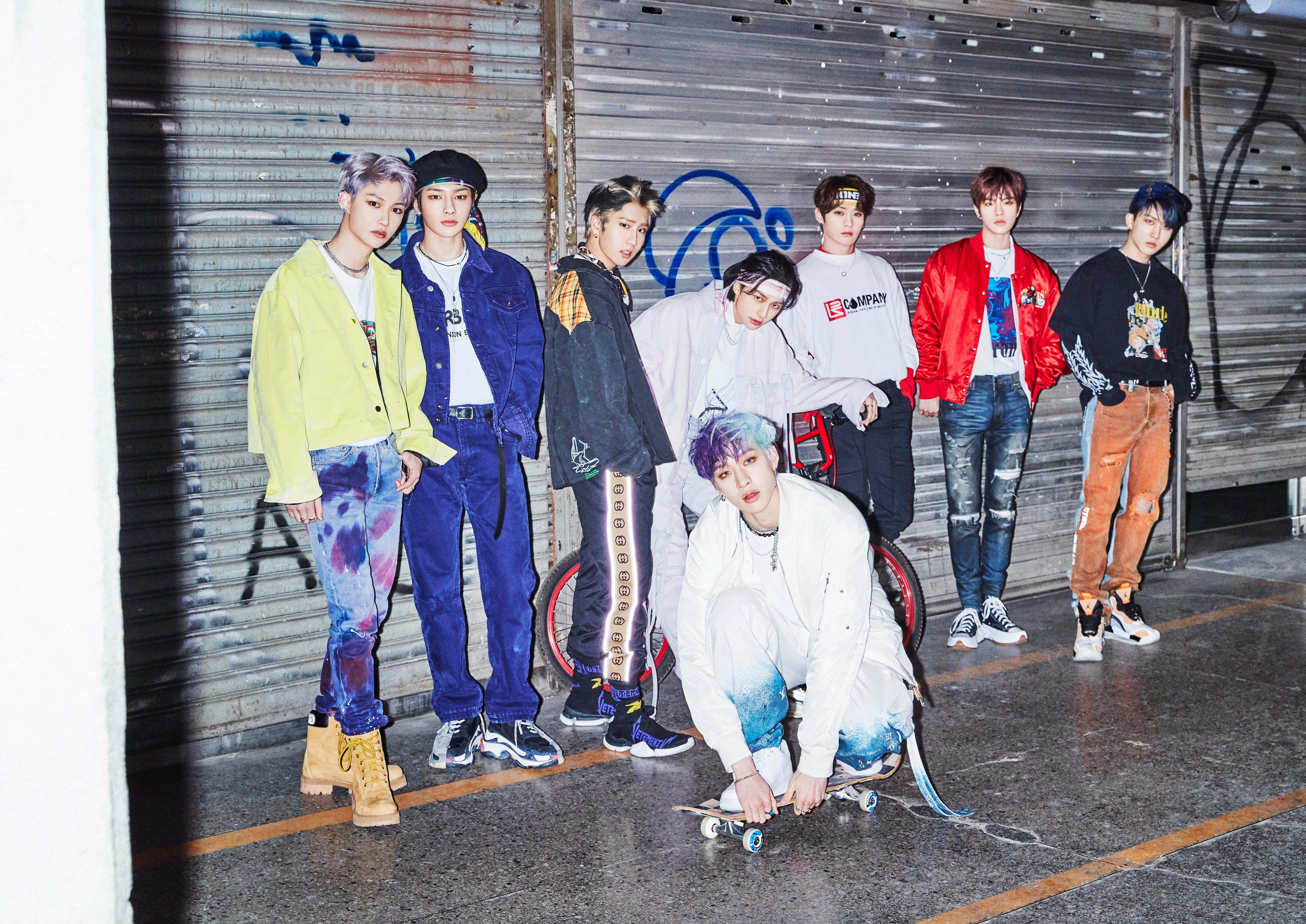 Stray Kids 2020 桌布 壁紙 — 七位時尚年輕男子穿著大膽街頭服飾，自信地在佈滿塗鴉的金屬百葉窗前擺姿勢，前景有一位滑板手。