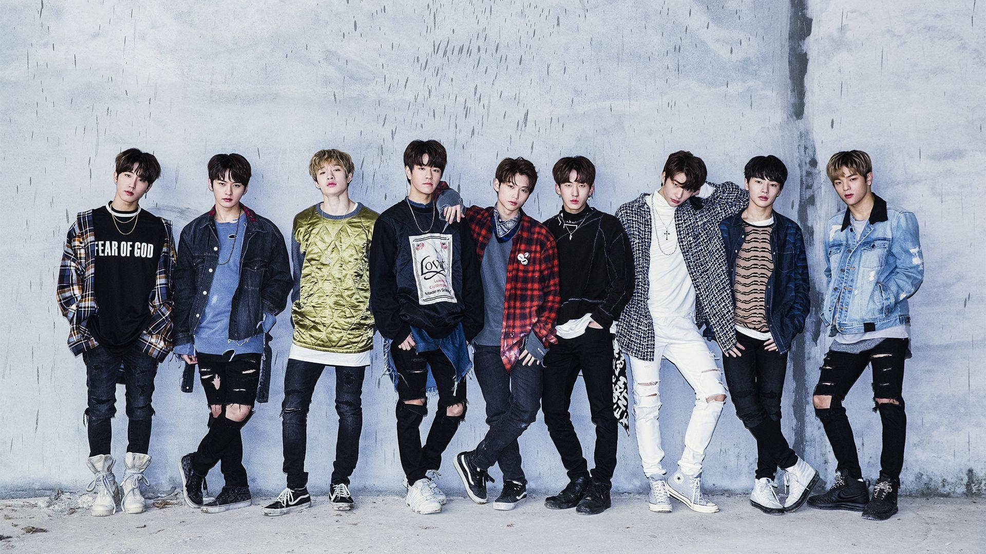Stray Kids 桌布 壁紙 — 七位時尚年輕男子穿著潮流街頭服飾，在雨中自信地擺姿勢，背景是帶紋理的灰色混凝土牆。
