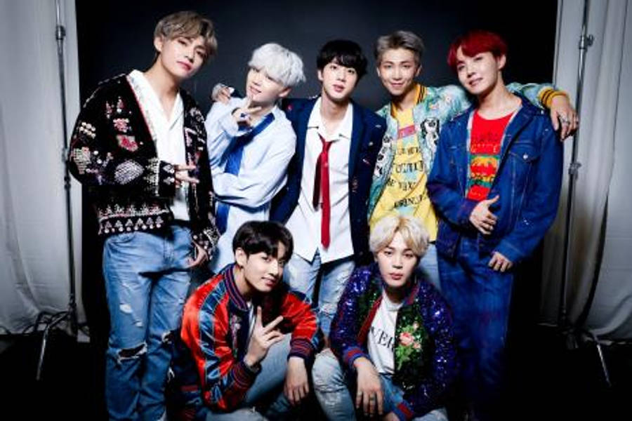 bts photoshoot 桌布 壁紙 — 七位時尚年輕男子穿著色彩繽紛的街頭服飾，在白色窗簾的深色工作室背景下自信地擺姿勢。