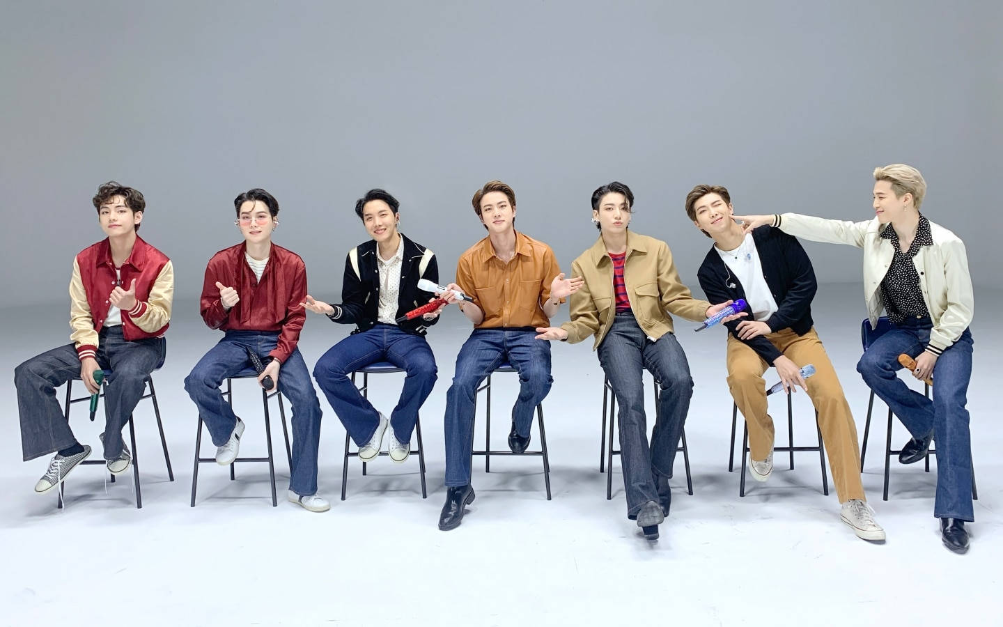 BTS 桌布 桌布 壁紙 — 七位時尚年輕男子身穿彩色外套和牛仔褲，休閒地坐在凳子上，背景是純灰色攝影棚。