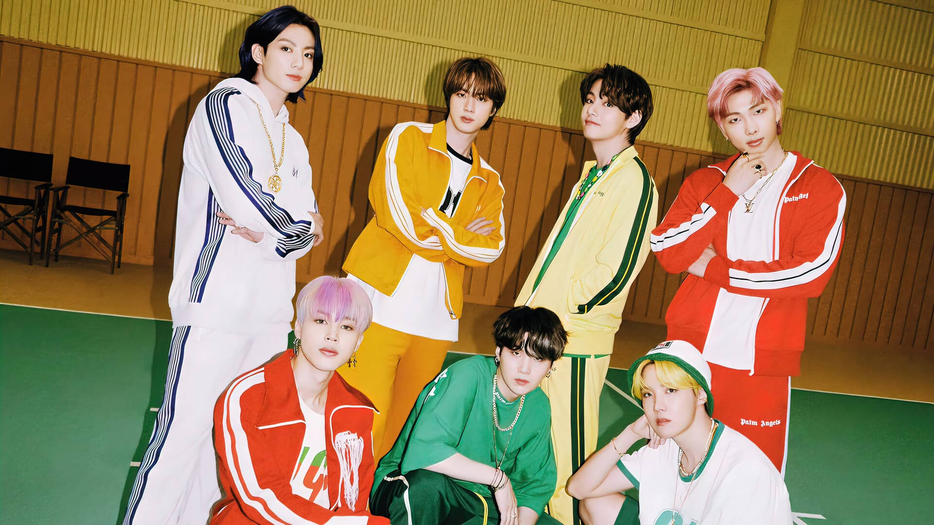 bts 2021 desktop 桌布 壁紙 — 七位時尚年輕男子身穿彩色運動服，在綠色健身房地板上對著木牆自信擺姿勢。
