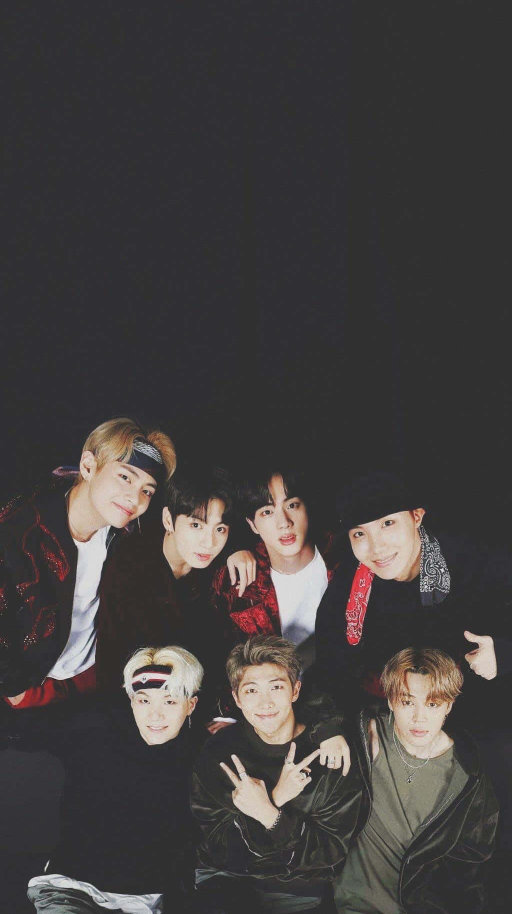 BTS 桌布 壁紙 — 七位時尚年輕男子身穿深色服裝，在黑色背景前緊密擺姿勢，表情俏皮。