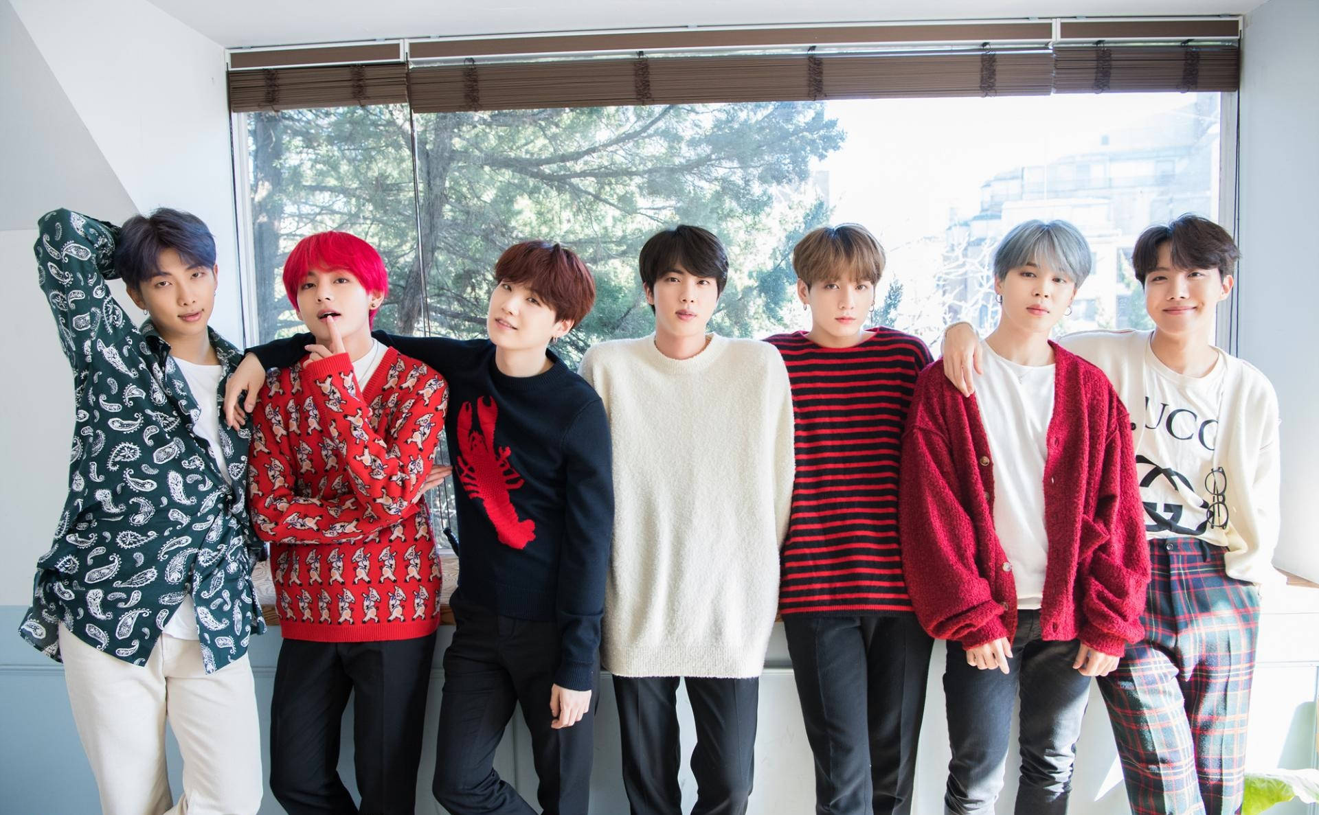 bts 2021 desktop 桌布 壁紙 — 七位時尚年輕男子身穿色彩繽紛的休閒服裝，在室內靠近一扇可以看到外面樹木的大窗戶旁一起擺姿勢。