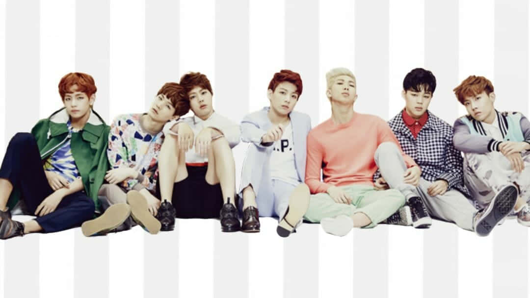 Cute Kpop 桌布 壁紙 — 七位時尚年輕男子身穿色彩繽紛的服裝，隨意地坐在大膽的白灰條紋背景前。
