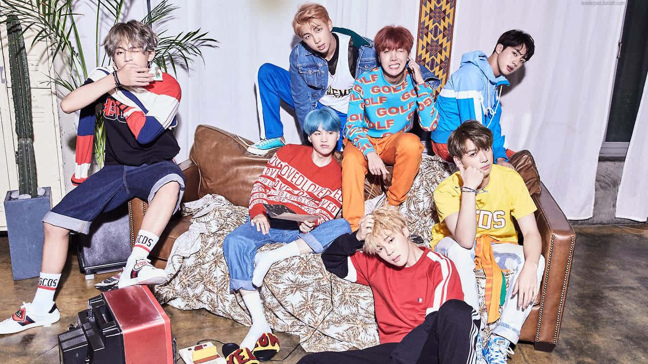 Bts Mac 桌布 壁紙 — 七位時尚年輕男子身穿色彩繽紛的街頭服飾，在現代室內環境中隨意地坐在棕色皮沙發上擺姿勢。