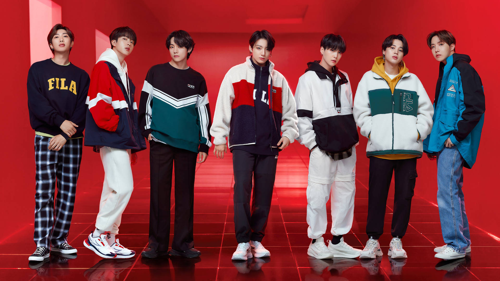 BTS 桌布 壁紙 — 七位時尚年輕男子身穿色彩繽紛的運動服，自信地站在帶有反射地板的發光紅色工作室背景前。