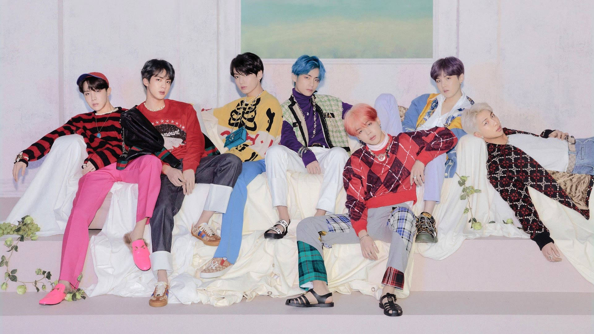 BTS 桌布 桌布 壁紙 — 七位時尚男士，擁有色彩繽紛的頭髮和大膽的服裝，在柔和的粉彩背景下，隨意地躺在一張白色布藝長椅上。