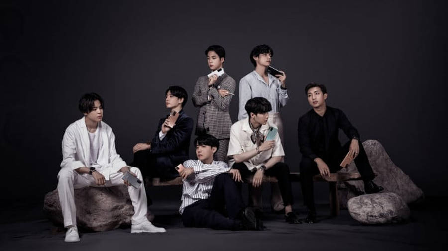 BTS 桌布 壁紙 — 七位時尚男士在黑暗的攝影棚背景下，隨意地坐在岩石和長椅上，手持麥克風和手機。