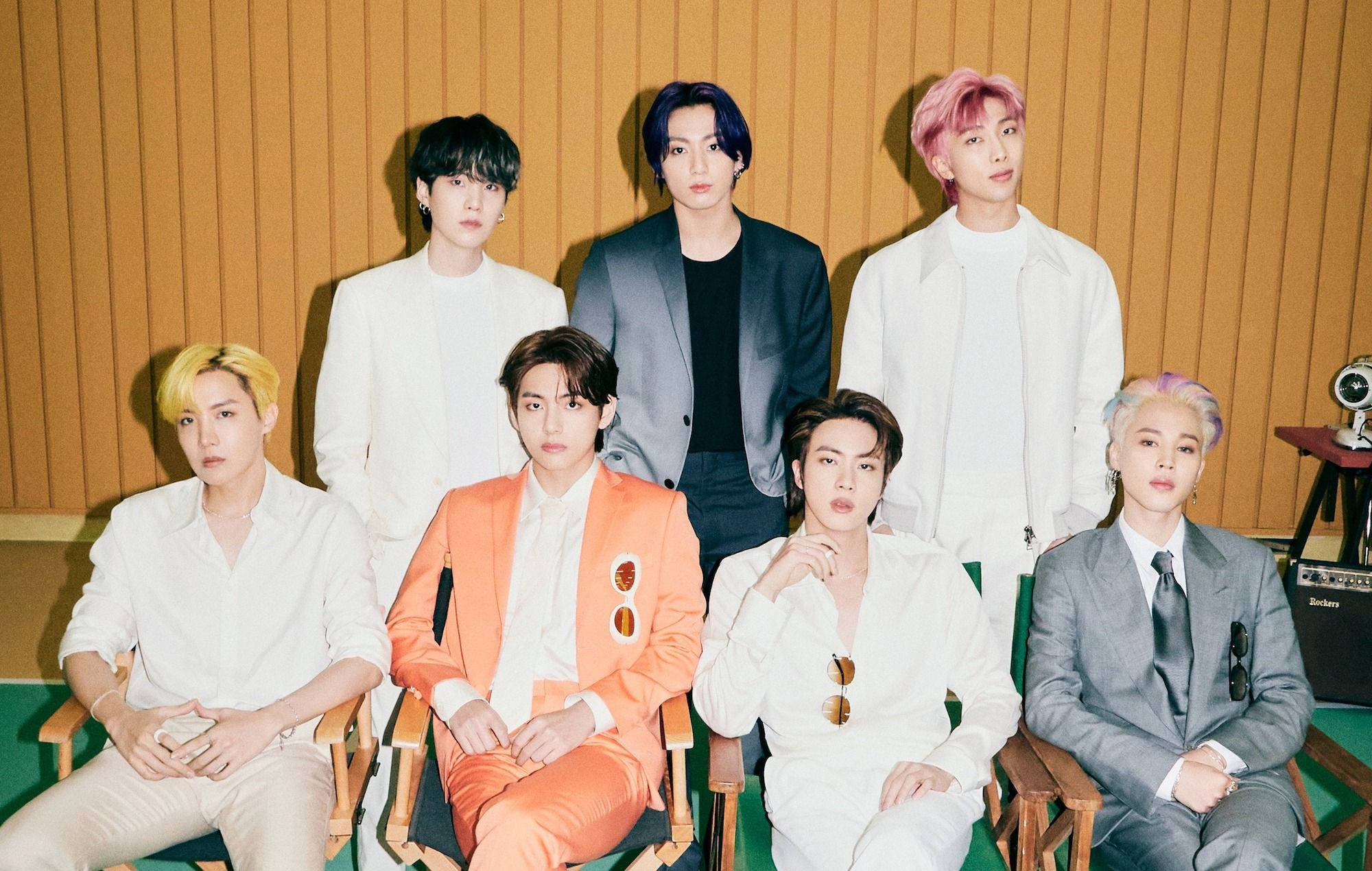 BTS 2021 桌布 壁紙 — 七位時尚男士擁有色彩繽紛的頭髮，自信地坐在導演椅上，背景是溫暖的木鑲板牆。