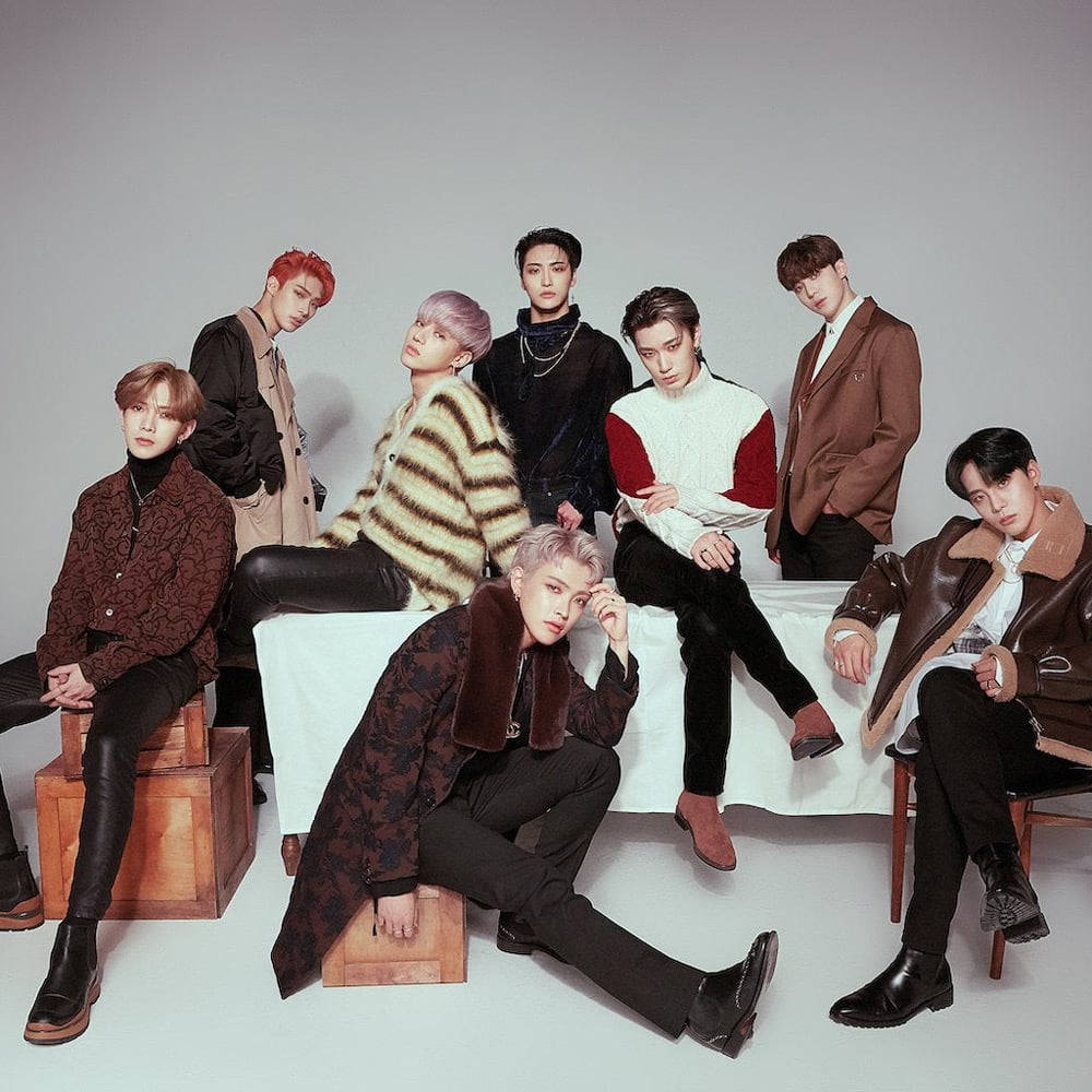 Kpop Aesthetic 桌布 壁紙 — 七位時尚男士擁有色彩繽紛的頭髮，自信地擺姿勢在木箱和椅子上，背景是純灰色的攝影棚。