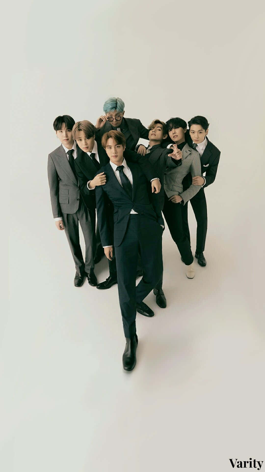 BTS 桌布 壁紙 — 七位時尚男士身穿俐落西裝，在極簡白色背景前自信擺姿勢，搭配戲劇性的頂光照明。