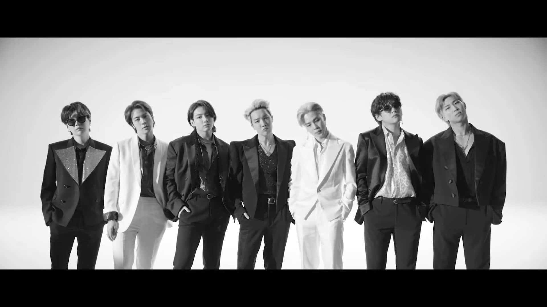 Bts Mv 桌布 壁紙 — 七位時尚男士身穿黑白西裝，在純色攝影棚背景前自信擺姿勢。