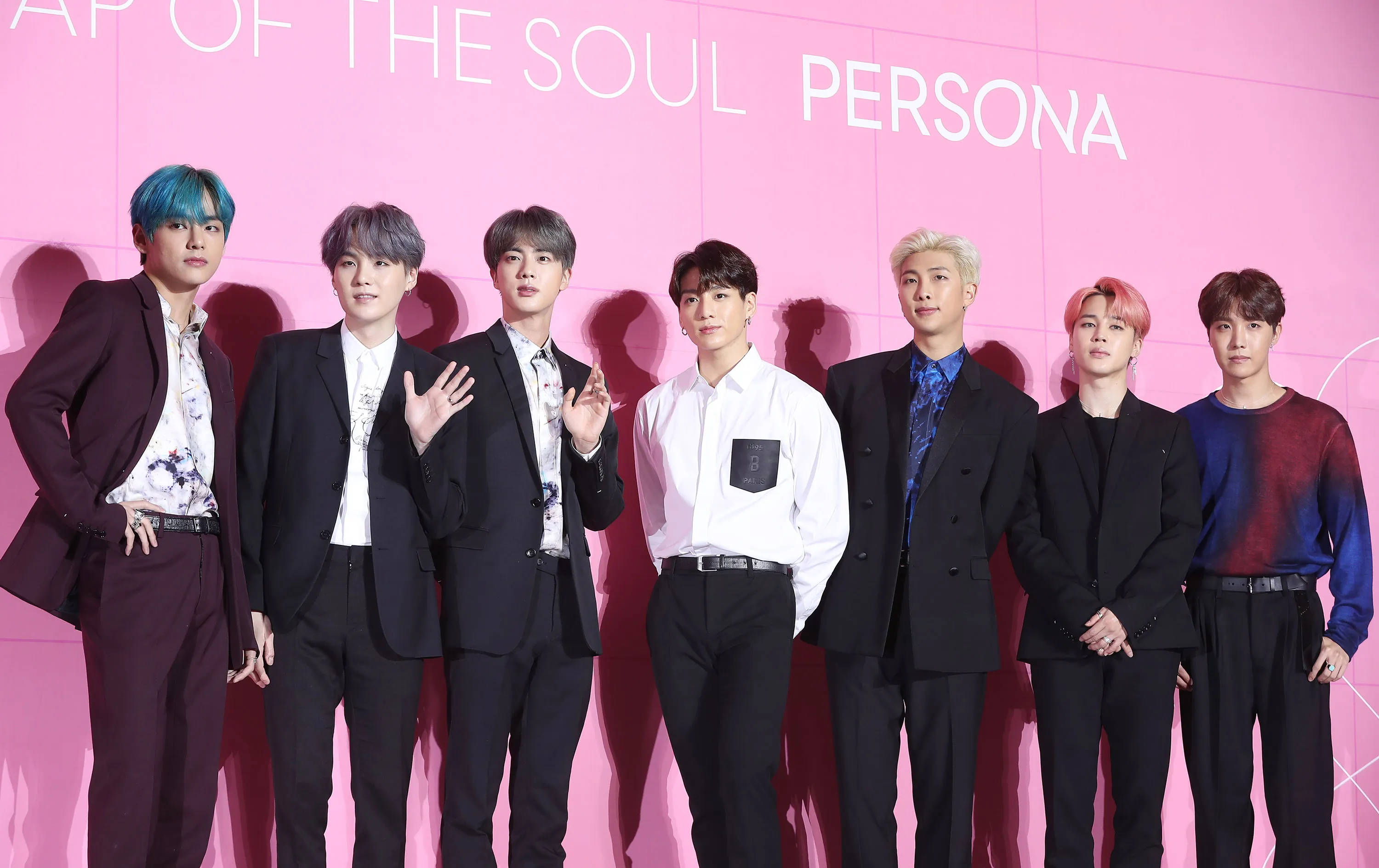 BTS 桌布 壁紙 — 七位時尚的K-pop偶像在帶有白色文字的鮮豔粉紅色背景前自信地擺姿勢。