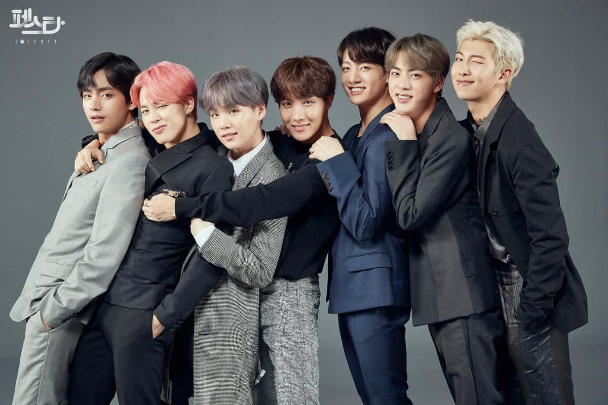 Bts Mac 桌布 壁紙 — 七位時尚的K-pop偶像穿著訂製西裝，在純灰色攝影棚背景前緊密擺姿勢，展現自信笑容和各種髮色。