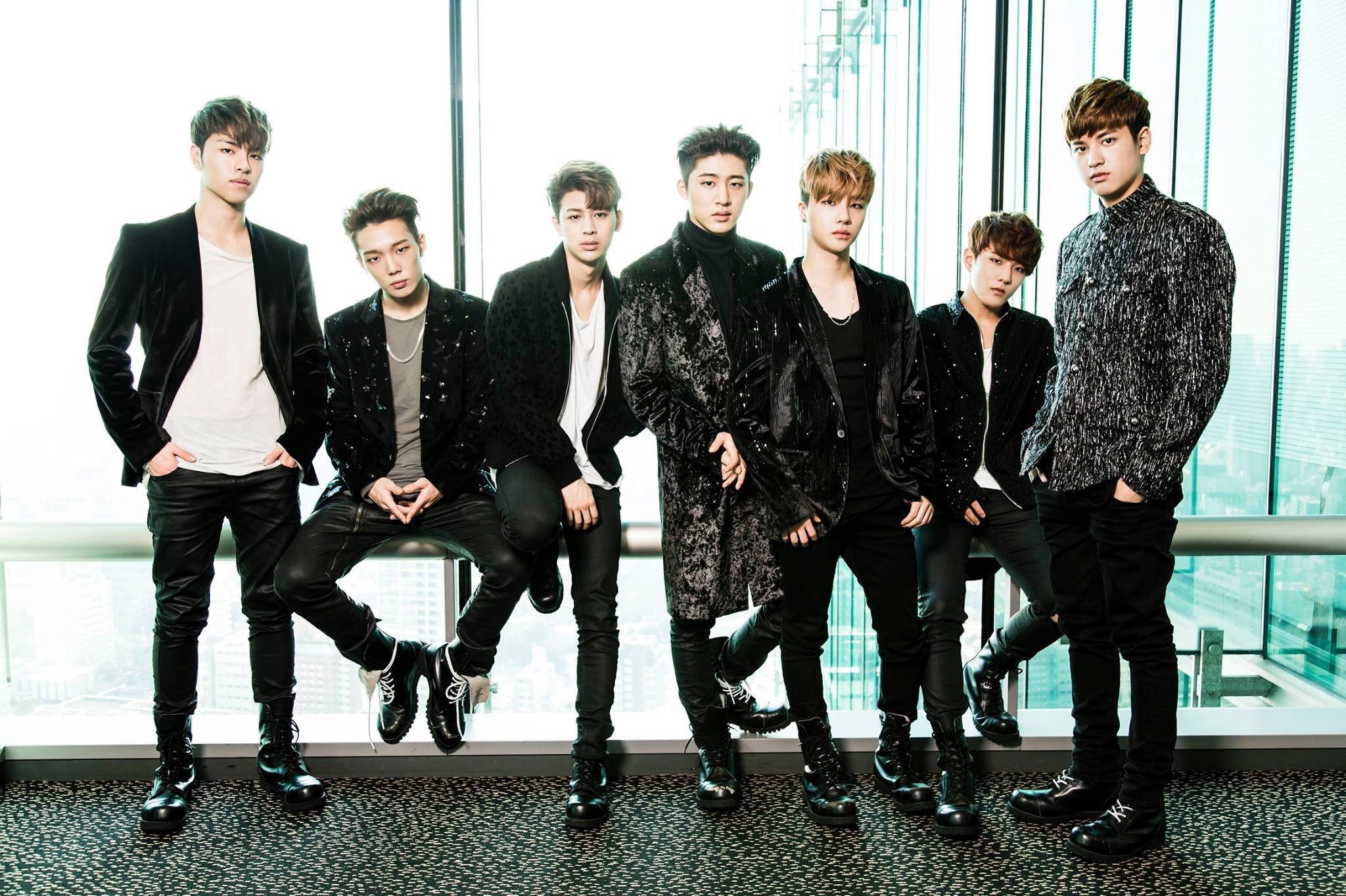 Ikon 桌布 壁紙 — 七位時尚的年輕男士穿著黑色天鵝絨和亮片服裝，在現代陽台上自信地擺姿勢，背景是城市天際線。