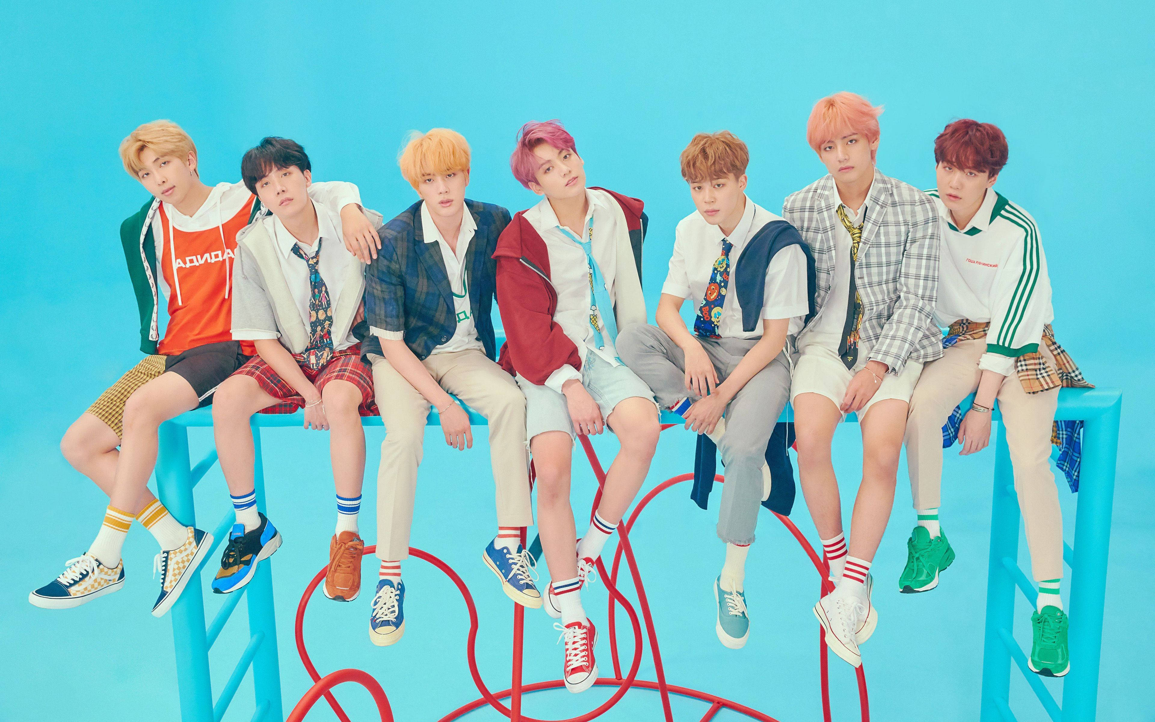 BTS 桌布 壁紙 — 七位時尚的年輕男子，頭髮色彩繽紛，隨意地坐在亮藍色的長椅上，背景是純青色。