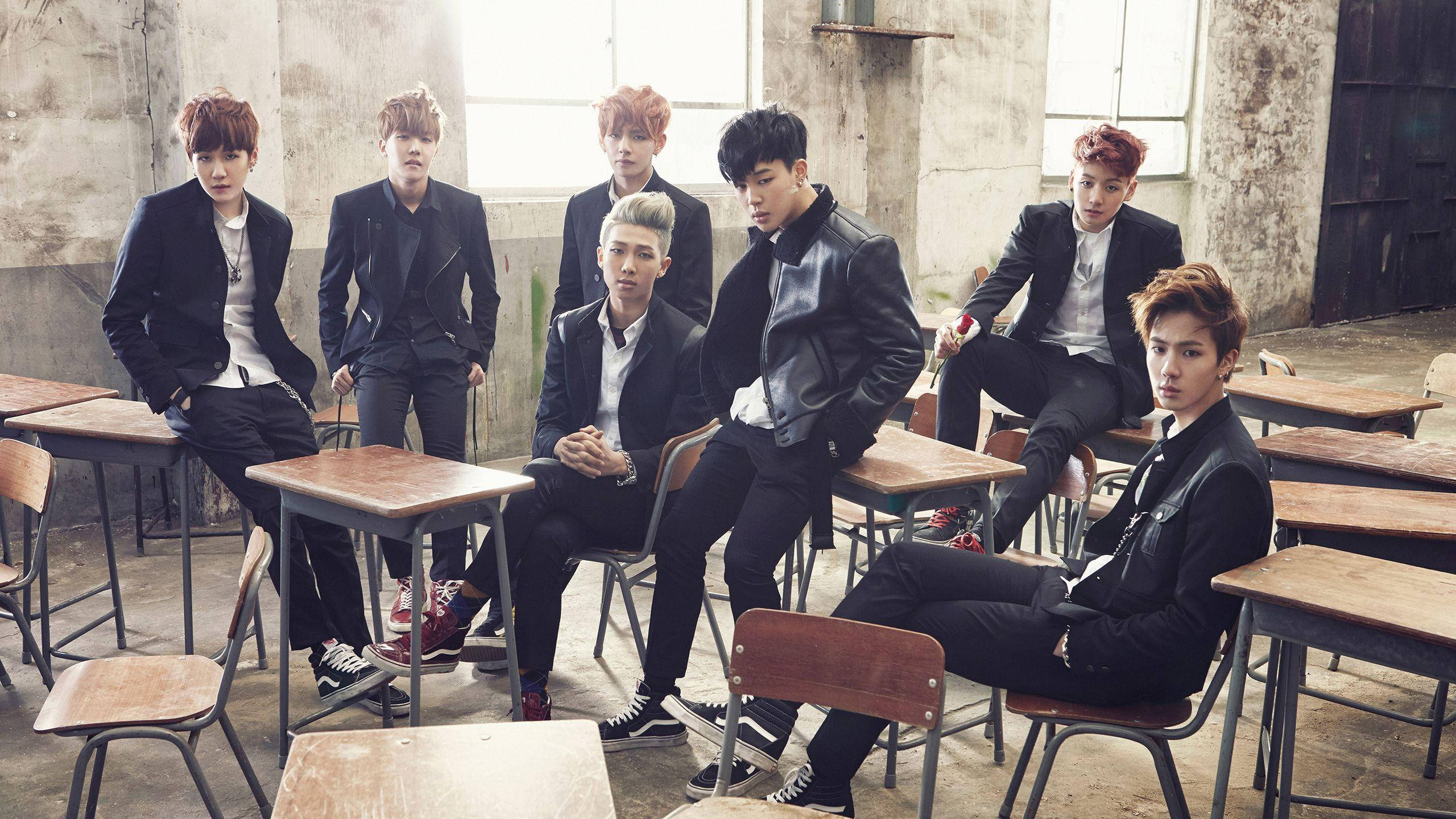 BTS 桌布 桌布 壁紙 — 七位時尚的年輕男子身穿黑色西裝，在破舊的廢棄學校教室桌椅和窗戶間自信地擺姿勢。