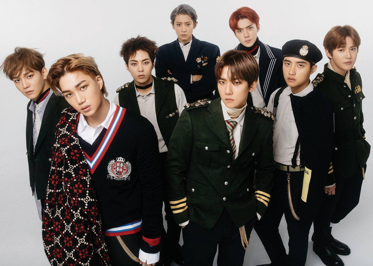 K-pop 桌布 壁紙 — 七位時尚的年輕男性穿著協調的軍事風格服裝，在純白色背景前自信地擺姿勢。
