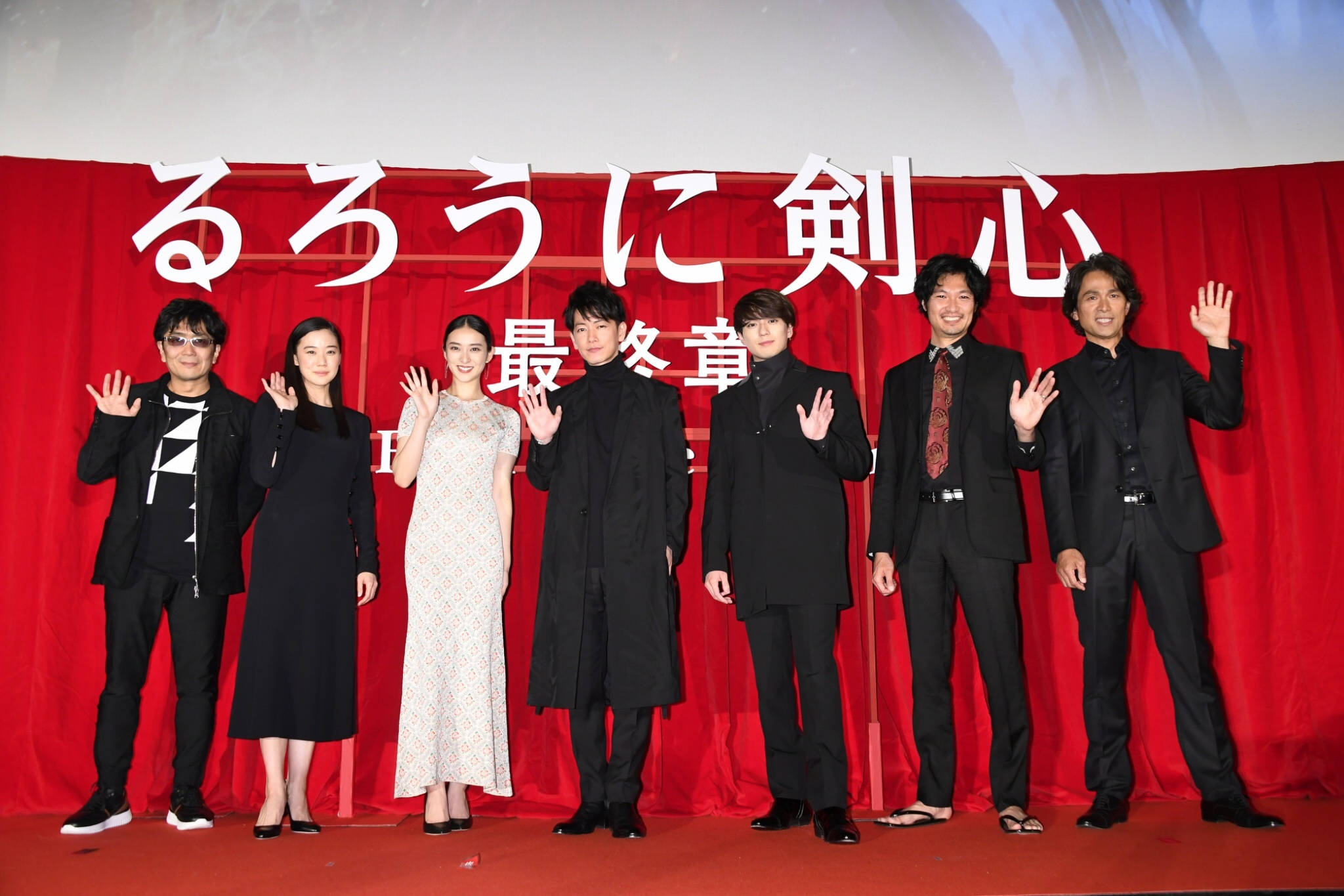 Kenshin 桌布 壁紙 — 七位演員在紅地毯上向鏡頭揮手，背景是帶有白色日文字的紅色窗簾。