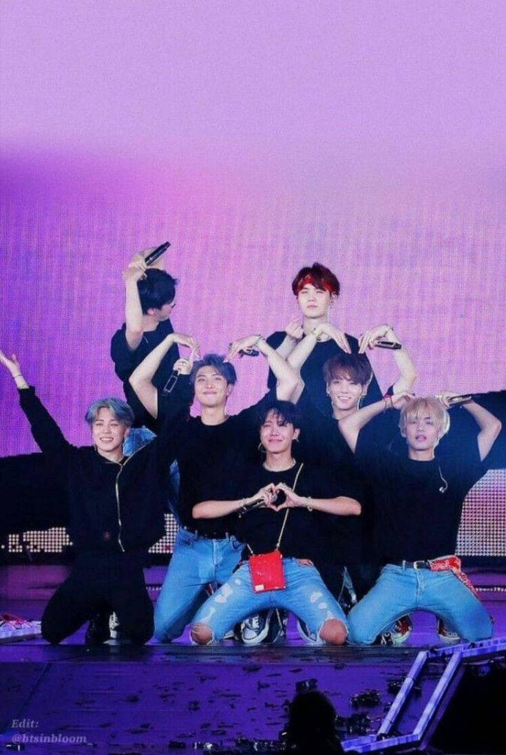 BTS 桌布 壁紙 — 七位男K-pop偶像在充滿活力的紫色燈光下在舞台上充滿活力地擺姿勢，用手形成心形。