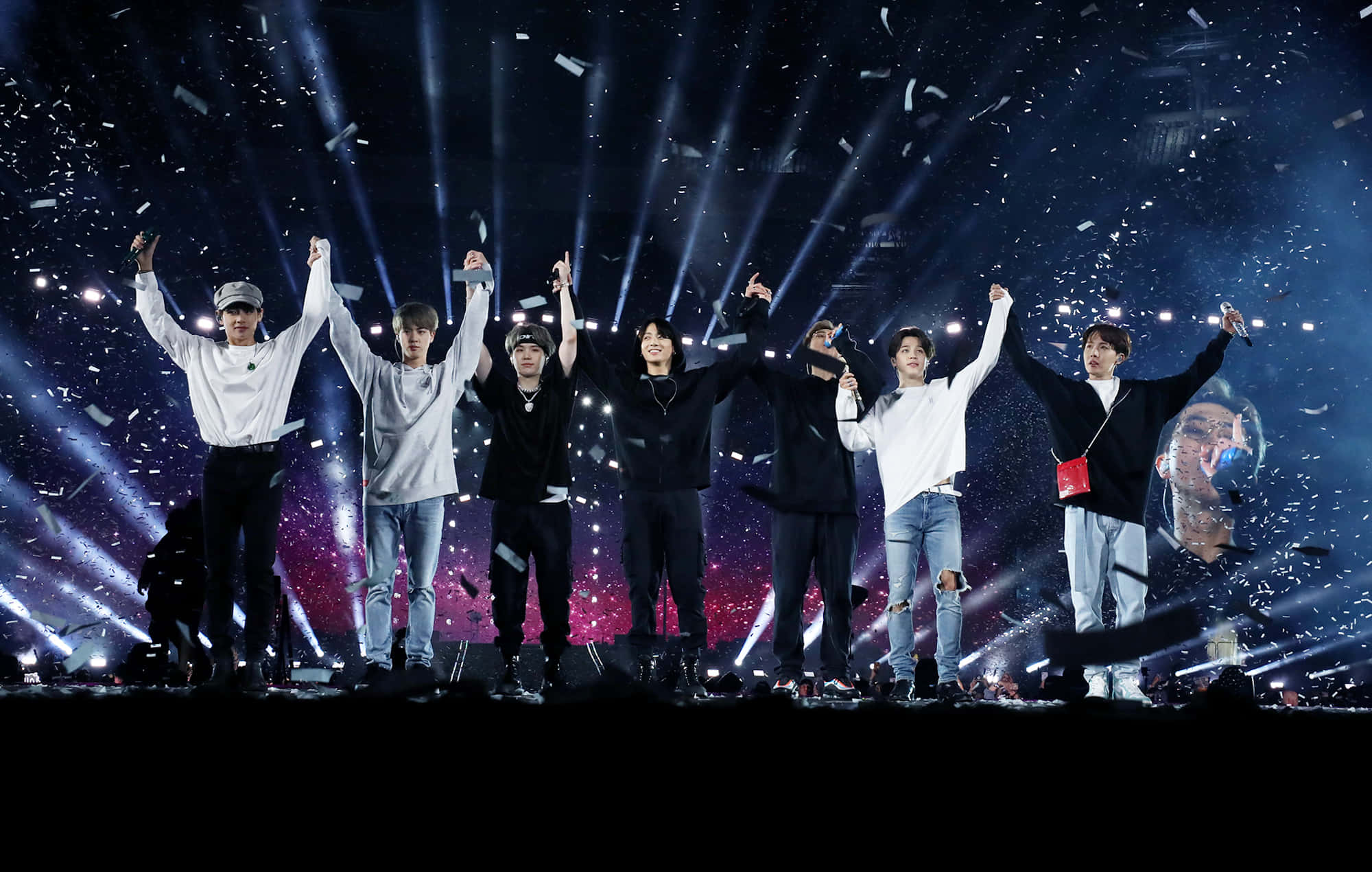 Bts Stage 桌布 壁紙 — 七位男表演者在一個耀眼的舞台上慶祝，五彩紙屑在明亮的聚光燈和宇宙背景下飄落。