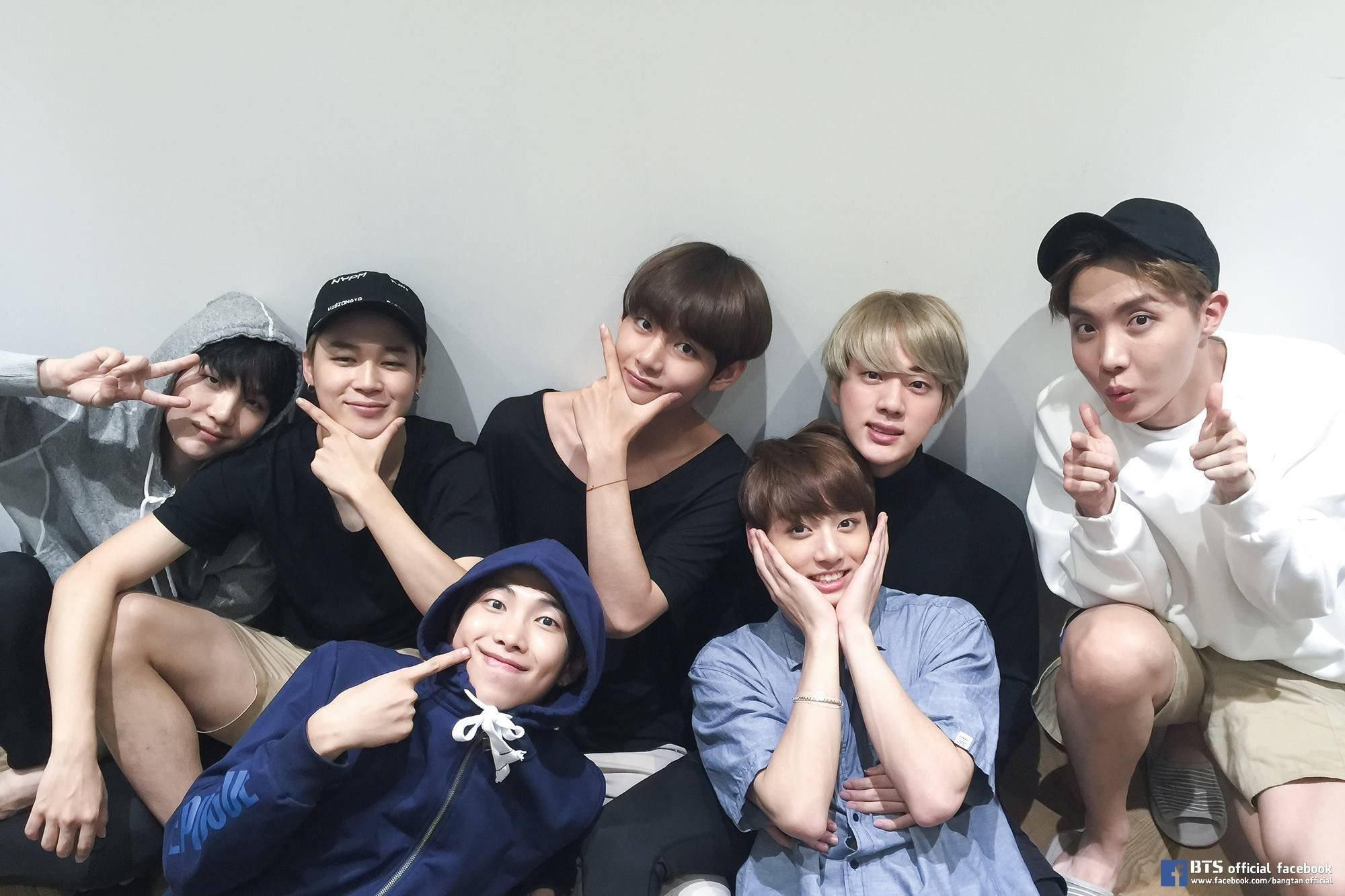 BTS 桌布 壁紙 — 七位穿著休閒服的年輕男子在純白牆前擺出有趣姿勢，做出和平手勢和鬼臉。