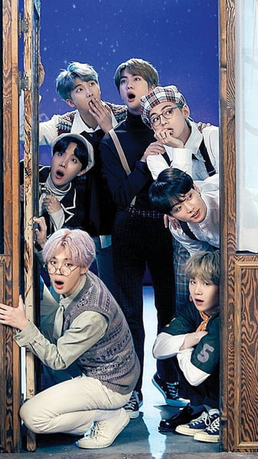 BTS 桌布 壁紙 — 七位穿著時尚的年輕男子，在繁星點點的夜空下，帶著驚訝的表情從木門後探頭窺視。
