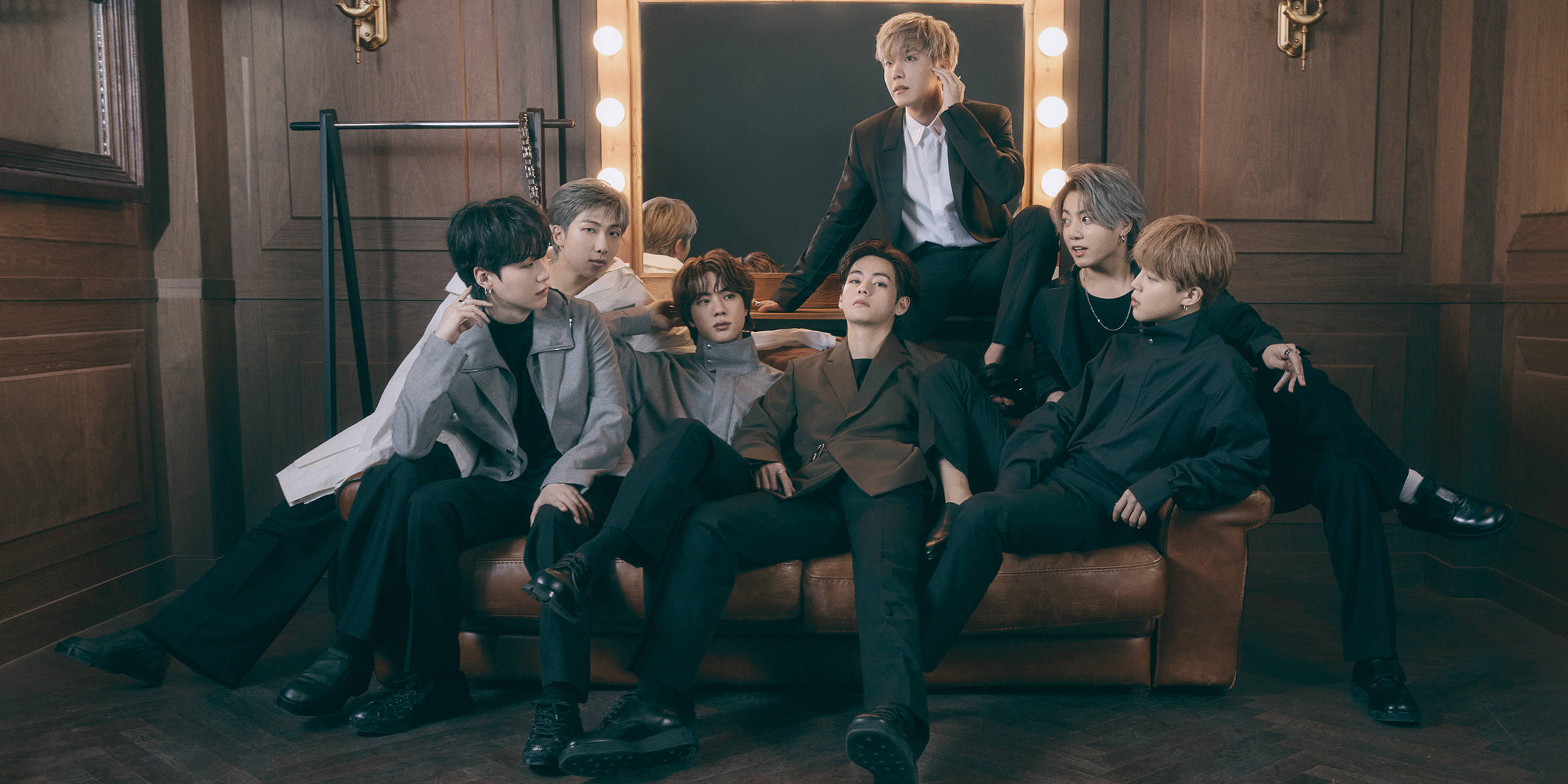 bts 2021 desktop 桌布 壁紙 — 七位穿著西裝的時尚男士在溫暖照明的木質房間裡，在化妝燈下自信地坐在皮革沙發上擺姿勢。