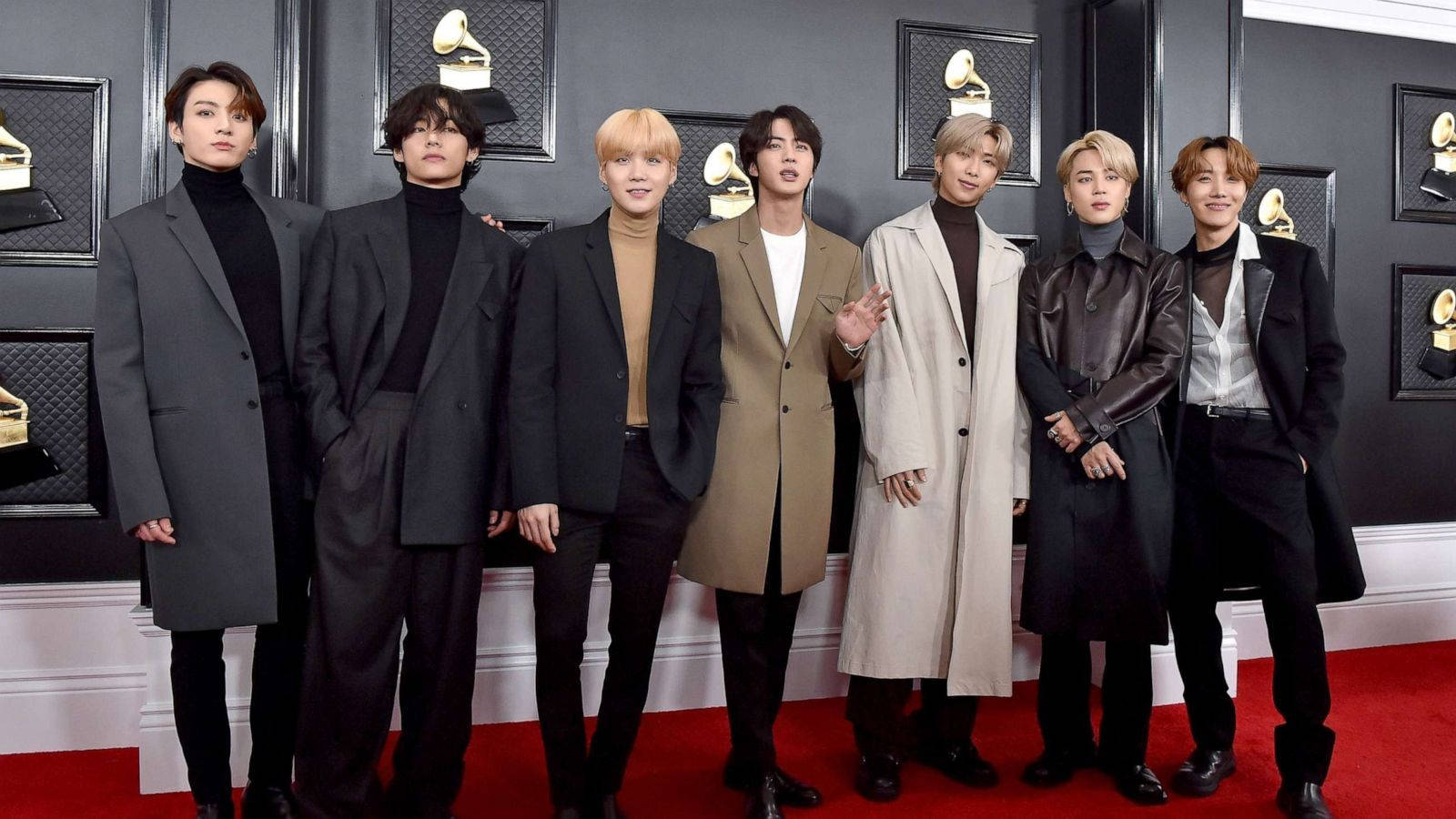 BTS 2021 桌布 壁紙 — 七位穿著訂製大衣的時尚男士在紅地毯上自信地擺姿勢，背景是裝飾著葛萊美獎獎盃的黑色牆壁。