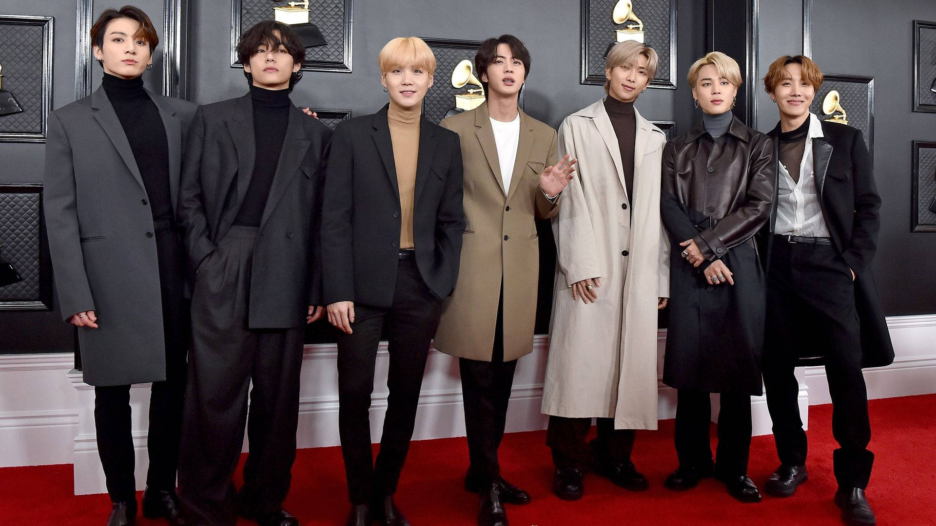BTS 桌布 桌布 壁紙 — 七位穿著訂製大衣的時尚男士在黑色牆壁前、金色葛萊美獎盃襯托下的紅地毯上自信地擺姿勢。