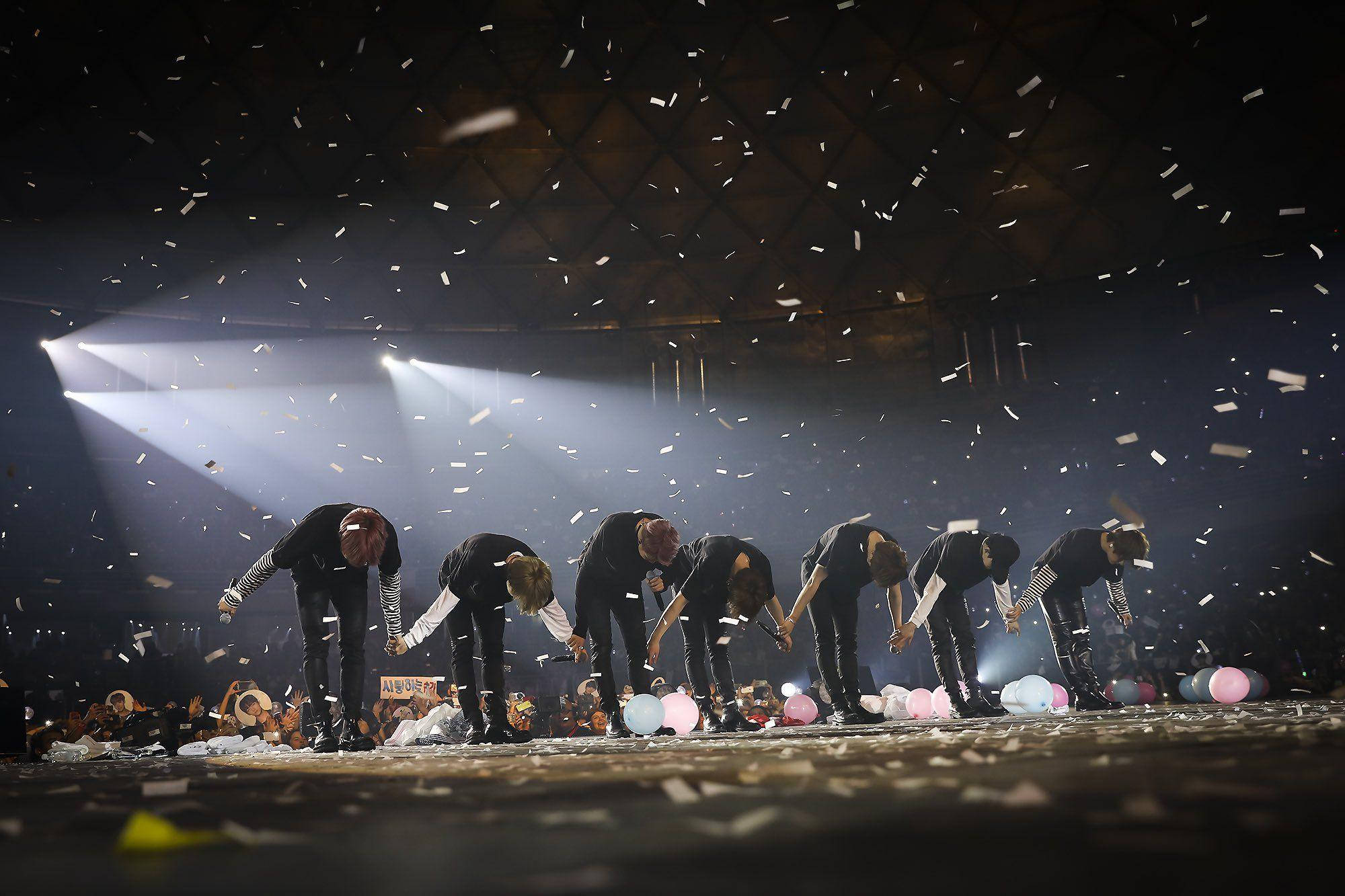 BTS 桌布 桌布 壁紙 — 七位表演者在明亮的聚光燈下，在紙屑如雨般落下的舞台上深深鞠躬。