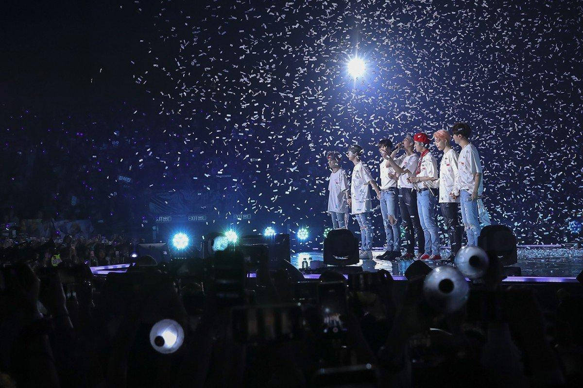 BTS 桌布 壁紙 — 七位表演者站在燈光明亮的舞台上，五彩紙屑如雨般灑落在黑暗的音樂會人群上。
