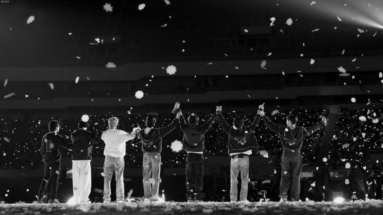 BTS 桌布 桌布 壁紙 — 七位表演者背光站在舞台上，雪花在他們周圍飄落，構成單色音樂會場景。