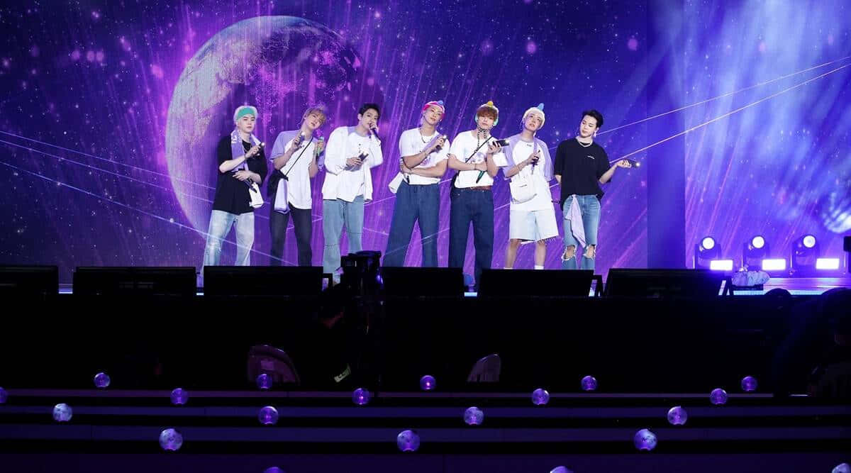 七位K-pop表演者在紫色燈光舞台上，背景是宇宙星球。 — 防彈少年團 合照 壁紙