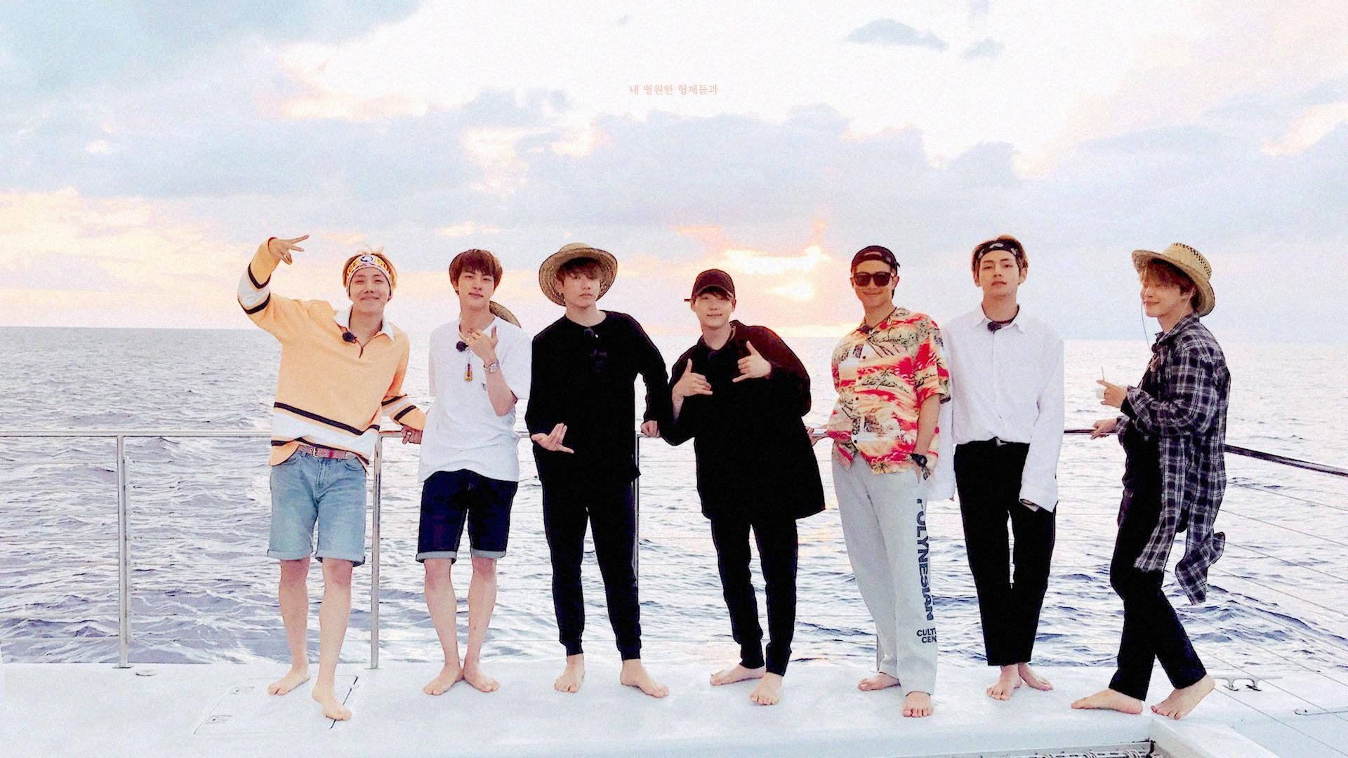 BTS 桌布 壁紙 — 七位身穿休閒夏日服裝的男士赤腳在船甲板上擺姿勢，背景是柔和的日落天空和寧靜的海洋。