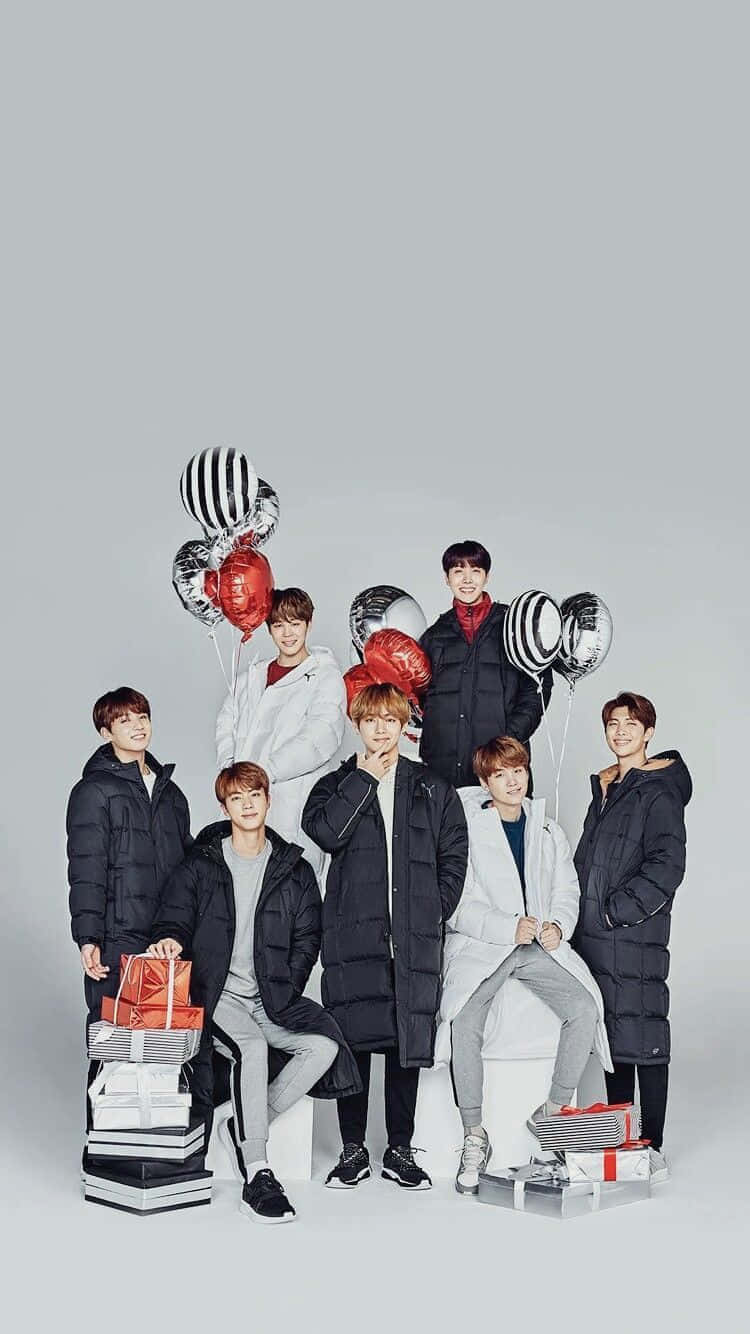 BTS 桌布 壁紙 — 七位身穿冬季外套的年輕男子，在純灰色背景前，手持紅色和銀色氣球及禮物盒擺姿勢。