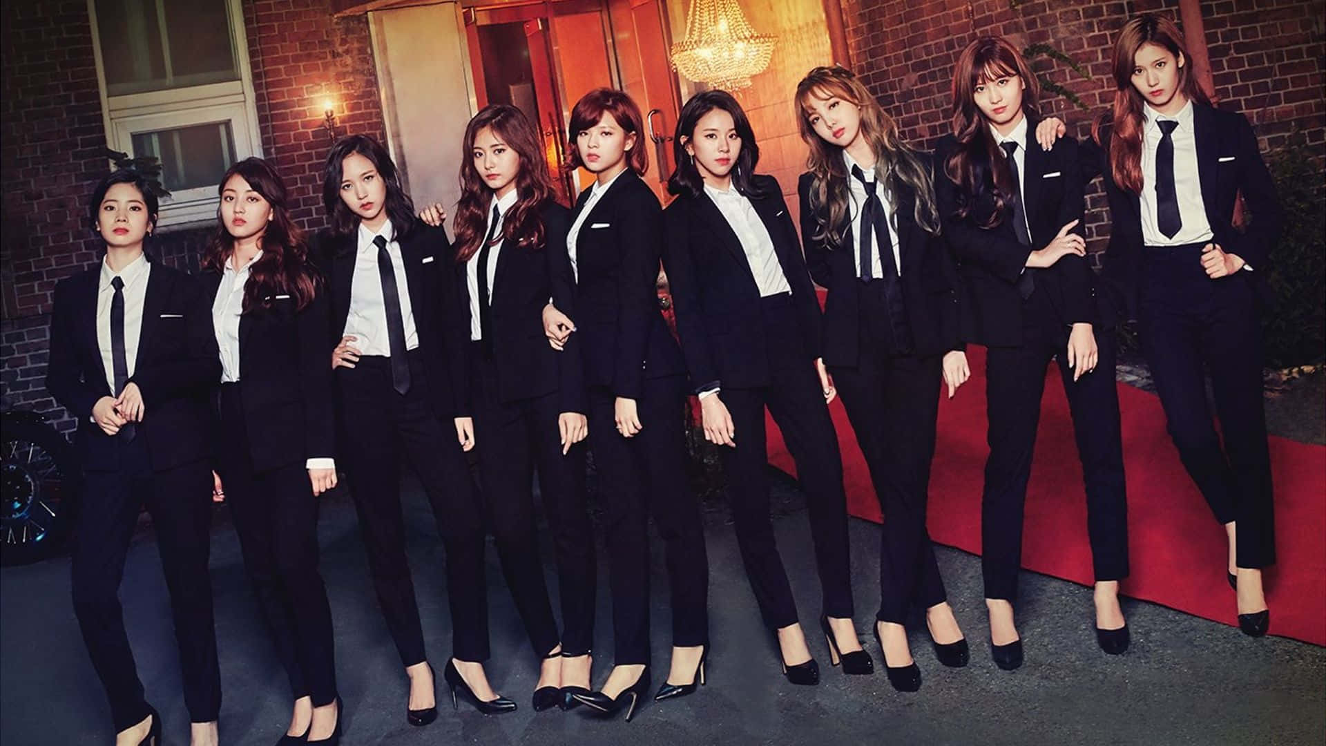 twice 桌布 壁紙 — 七位身穿利落黑色西裝和白色襯衫的女性在紅地毯上自信地擺姿勢，背景是磚牆。