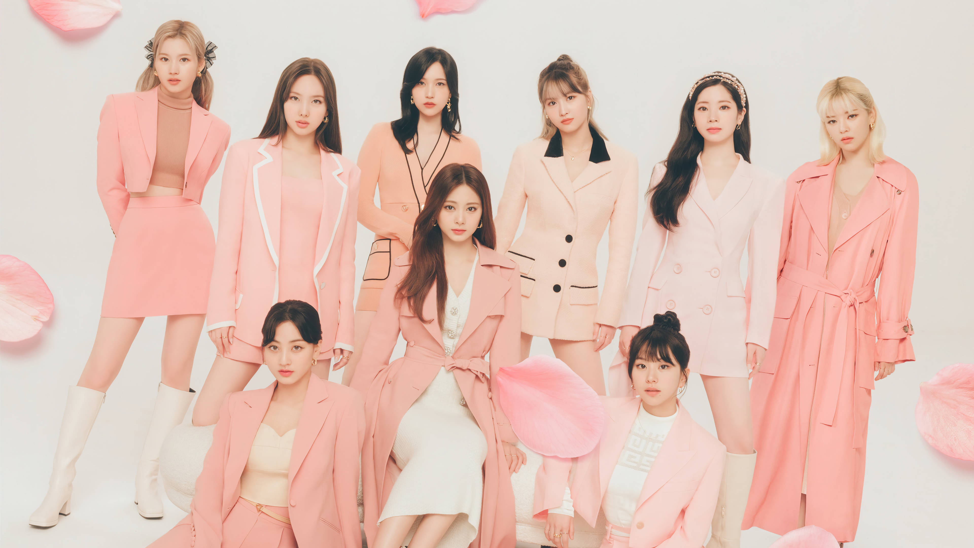 Kpop Aesthetic 桌布 壁紙 — 七位身穿協調粉色服裝的女性在白色背景前自信地擺姿勢，周圍飄浮著粉色花瓣。